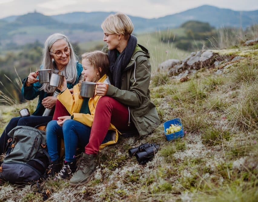 Three generations of a family sharing a flask of tea on a hillside