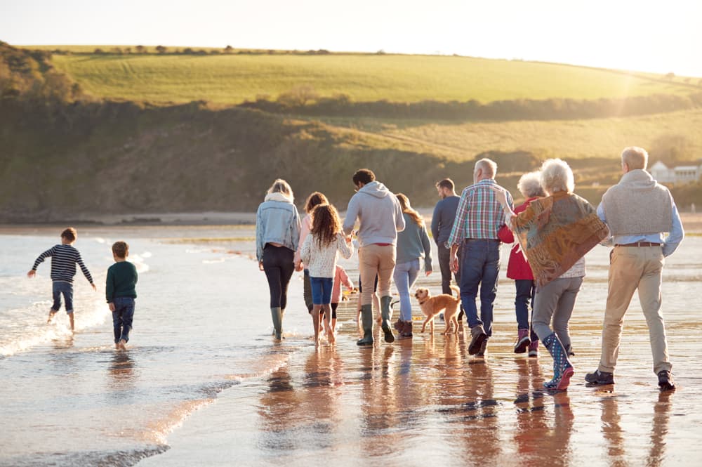 Three generations of a family walking together along a beach at sunset