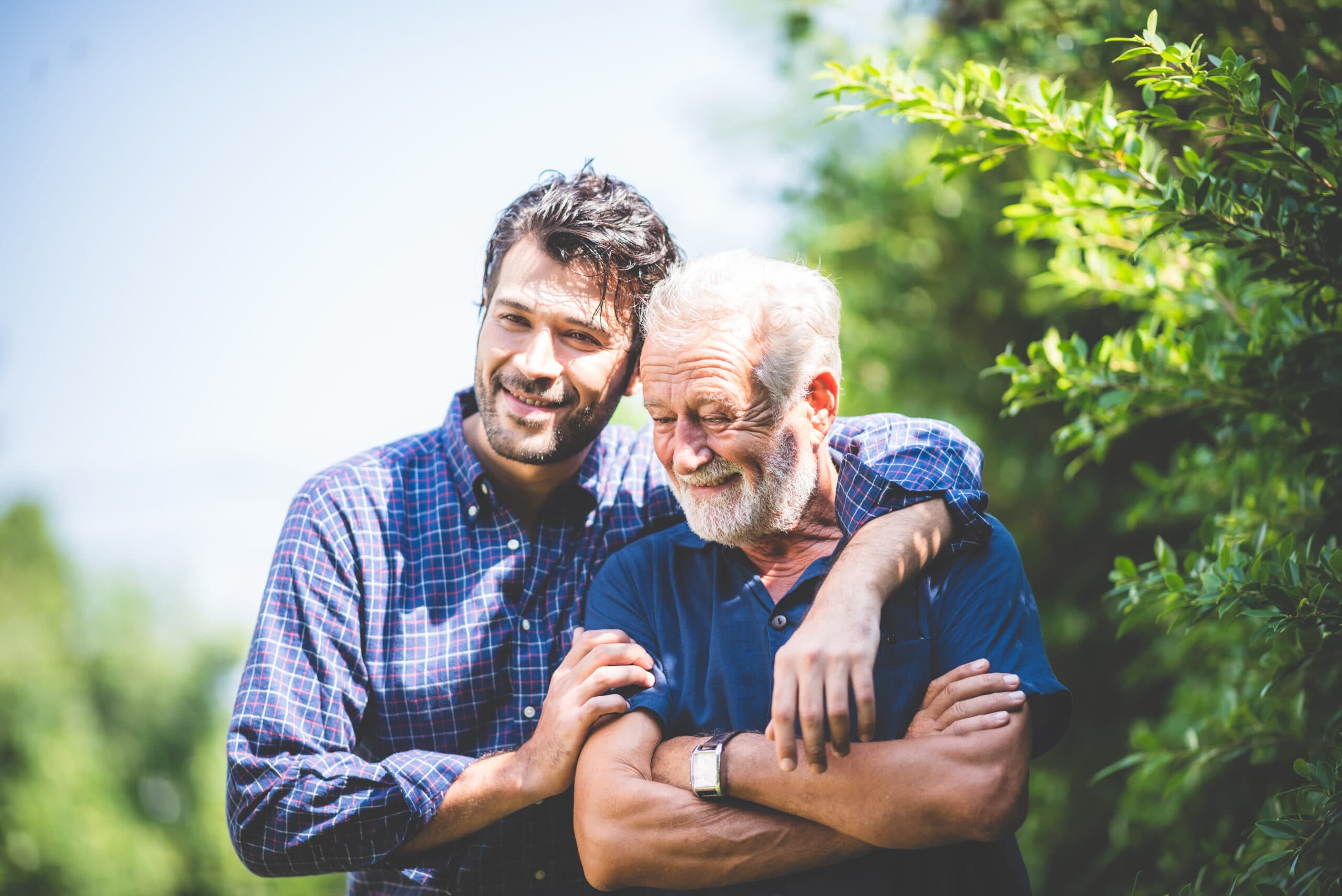 A smiling son with his arm around his elderly father outdoors