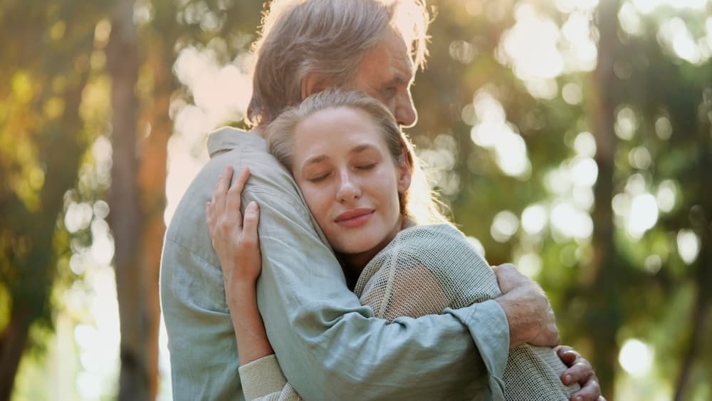 A father and daughter hugging in sunlit woodland